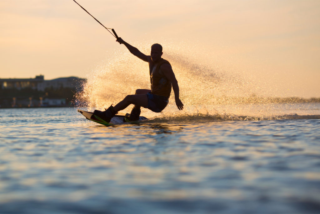 Personne pratiquant le wakeboard au coucher du soleil derrière un bateau